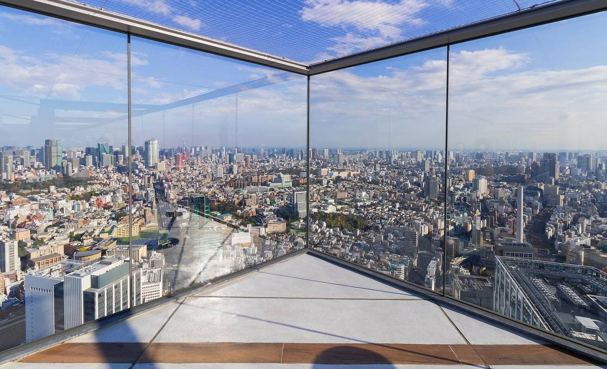 A glass-walled rooftop deck looking out over Tokyo under a blue sky