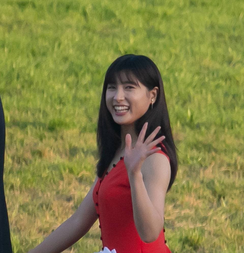 Tao Tsuchiya in a red dress, smiling and waving on a racecourse lawn