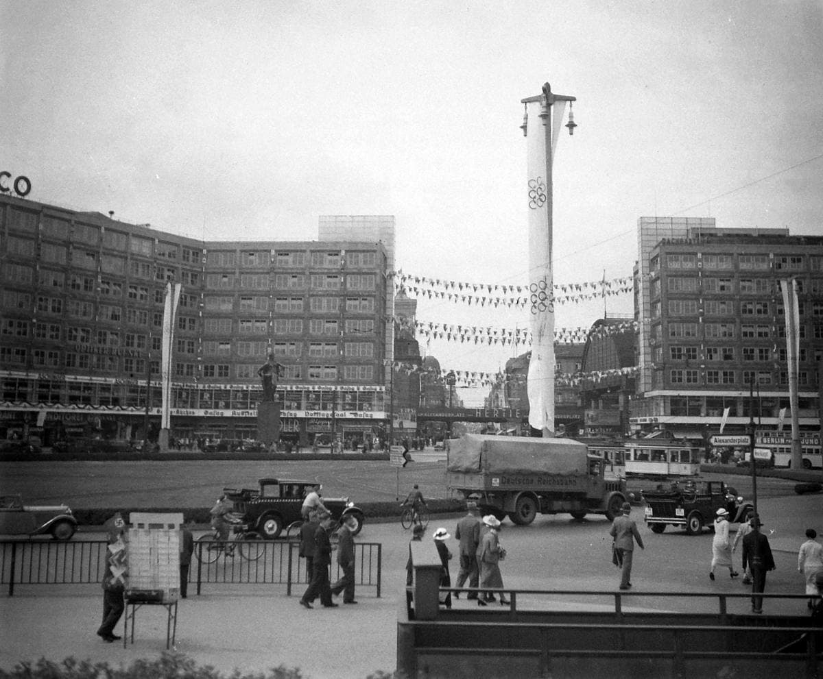 A black-and-white square with two long modern office blocks, cars and a tall pole hung with bunting