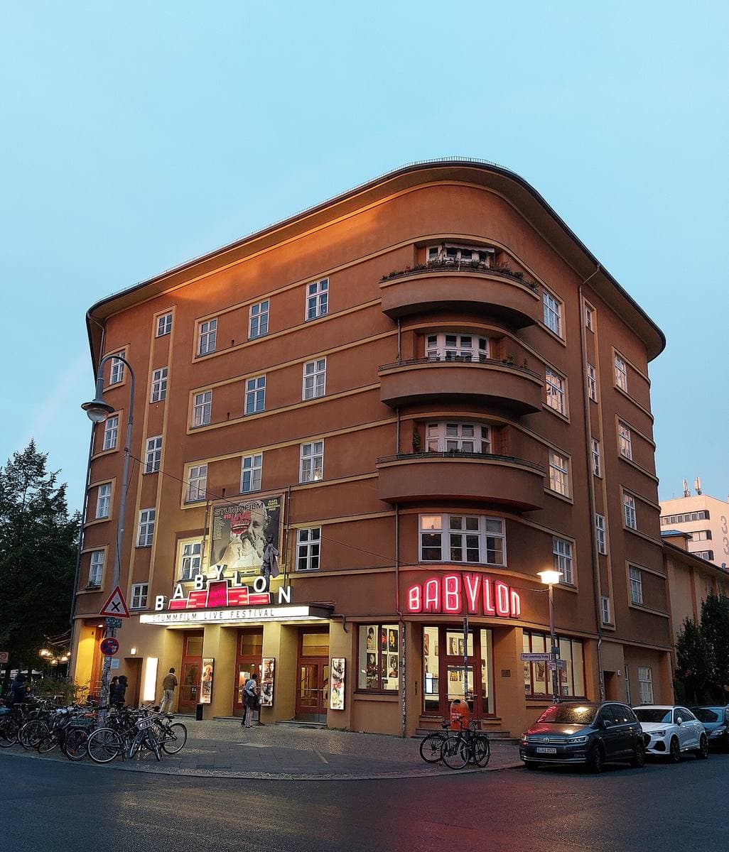 A rounded brick corner building with a lit BABYLON sign at dusk