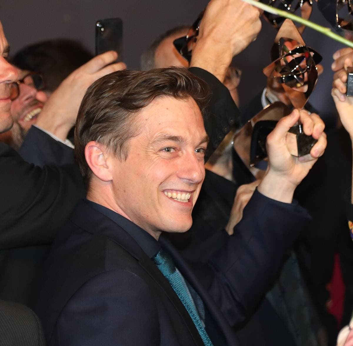 Volker Bruch laughing among a crowd holding up award trophies