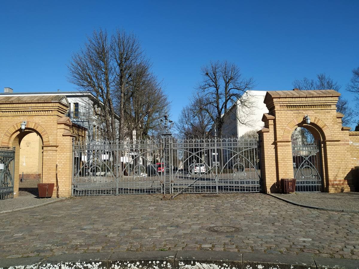 A yellow-brick gateway with iron gates and bare trees
