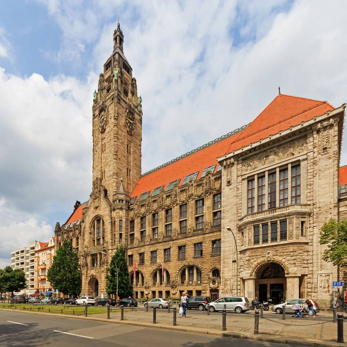 A sandstone town hall with a tall tower on a street corner