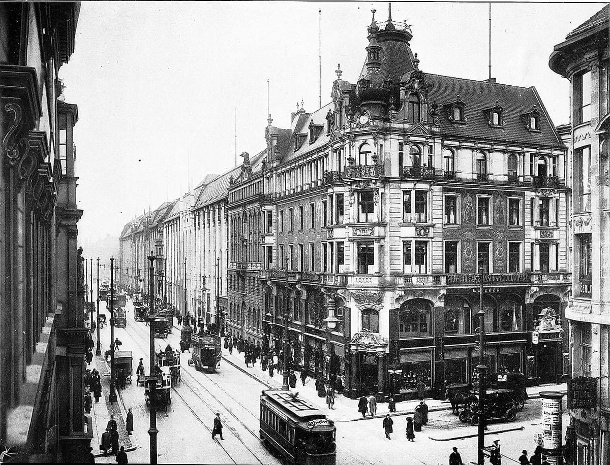 A black-and-white busy city corner with an ornate domed building, trams and crowds