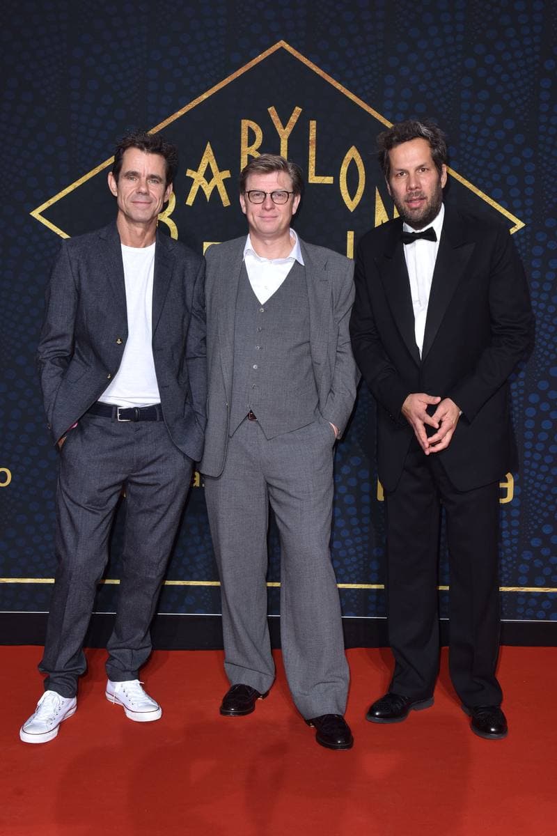 Three men in suits standing on a red carpet in front of a dark backdrop
