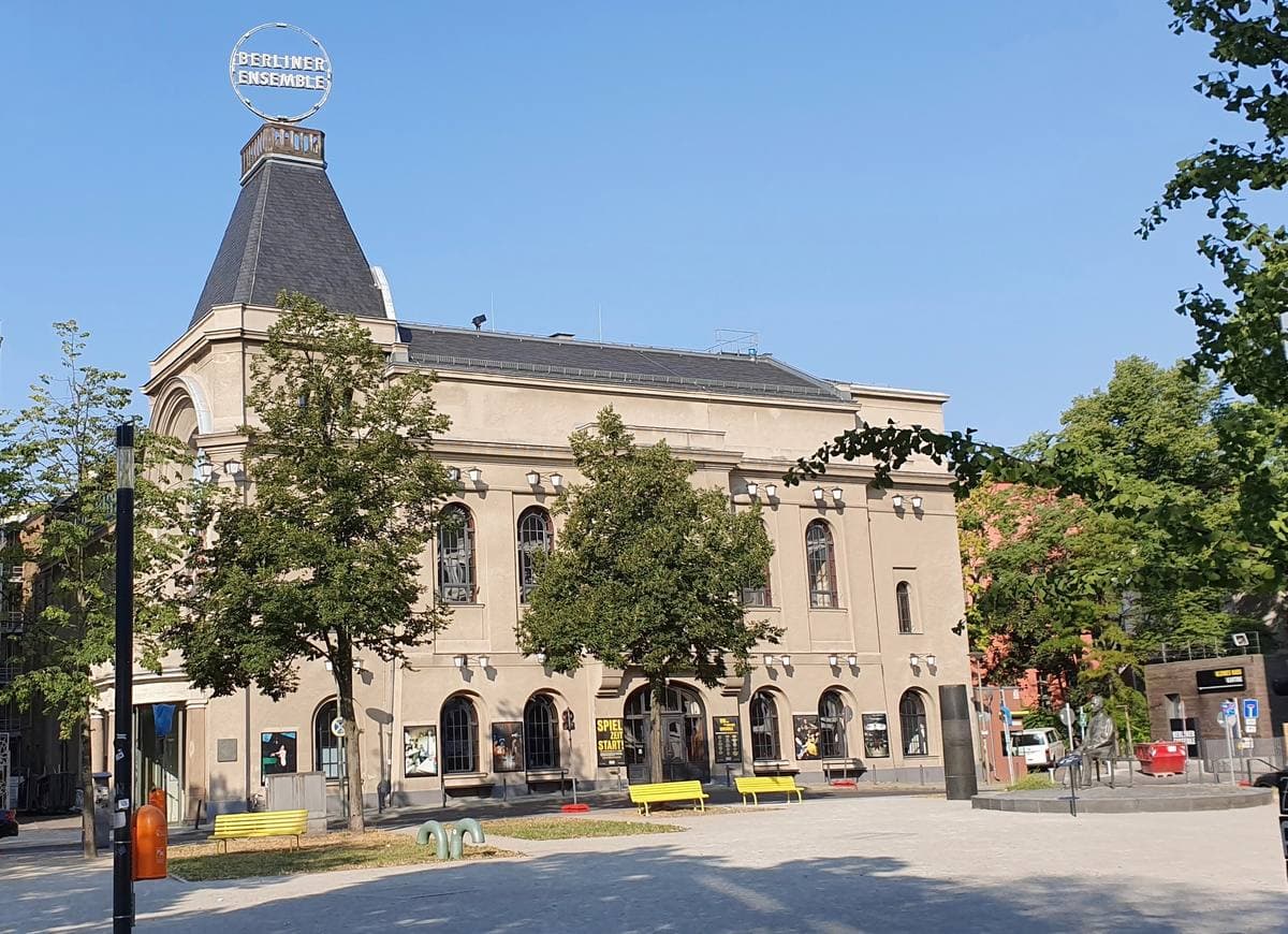 A theatre with a tall slate roof and a lit sign on top, among trees