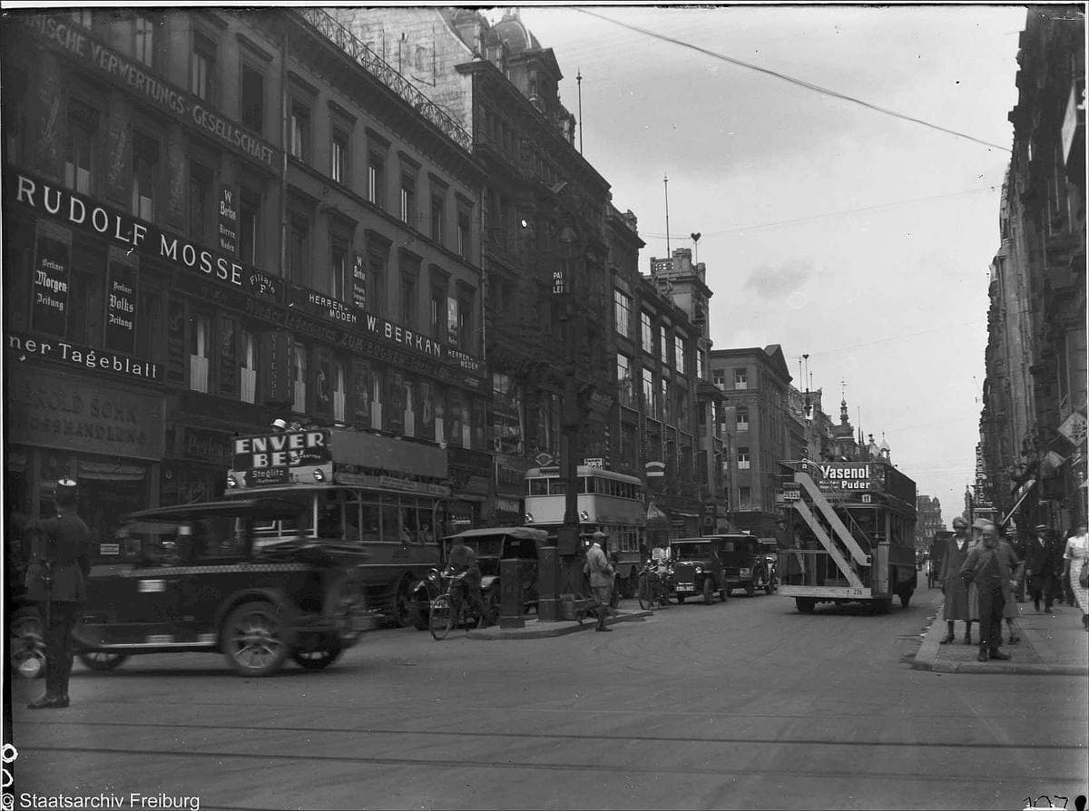 A black-and-white street of shop signs, motor cars and a double-decker bus