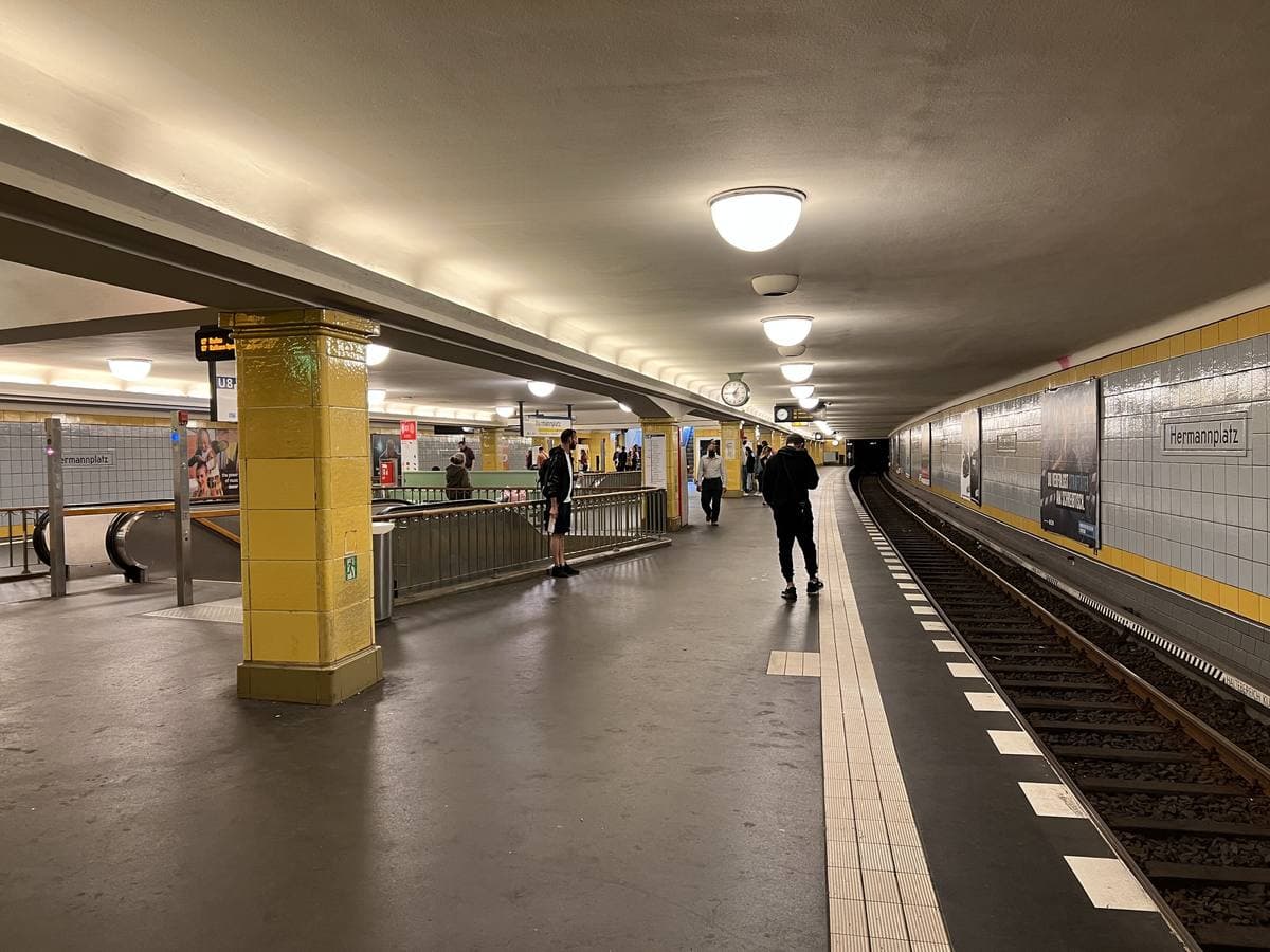 A long underground platform with yellow pillars and round ceiling lamps