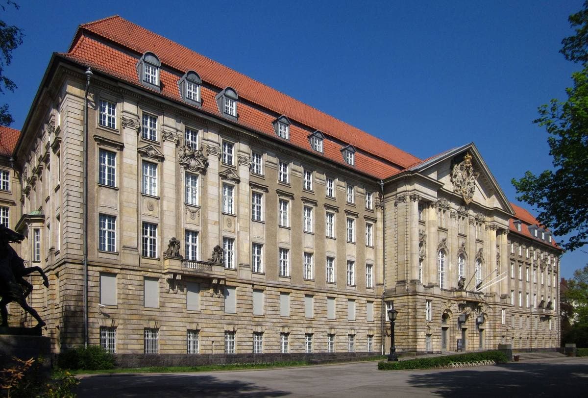 A long baroque-style court building behind a lawn and trees