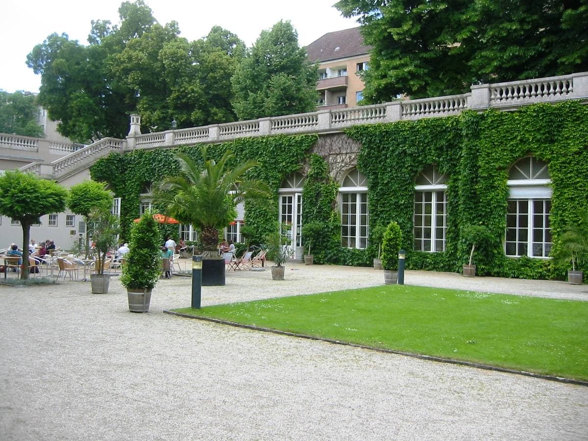 An ivy-covered orangery with tall windows above a gravel terrace