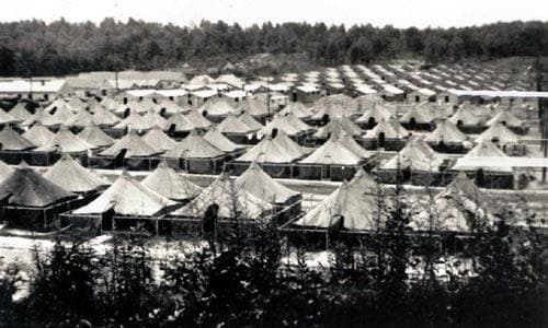 Rows of wooden army huts below a wooded hill