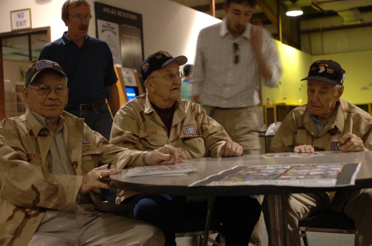 Three elderly veterans in caps sitting side by side