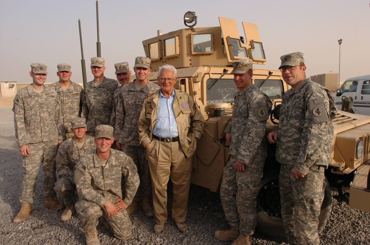 Don Malarkey, in a cap, with soldiers in front of an armoured truck