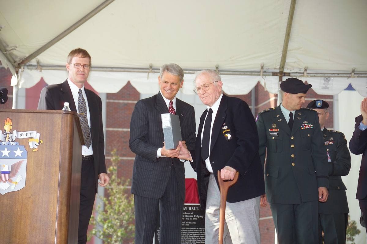 Dick Winters, seated, handing over a folder at a ceremony