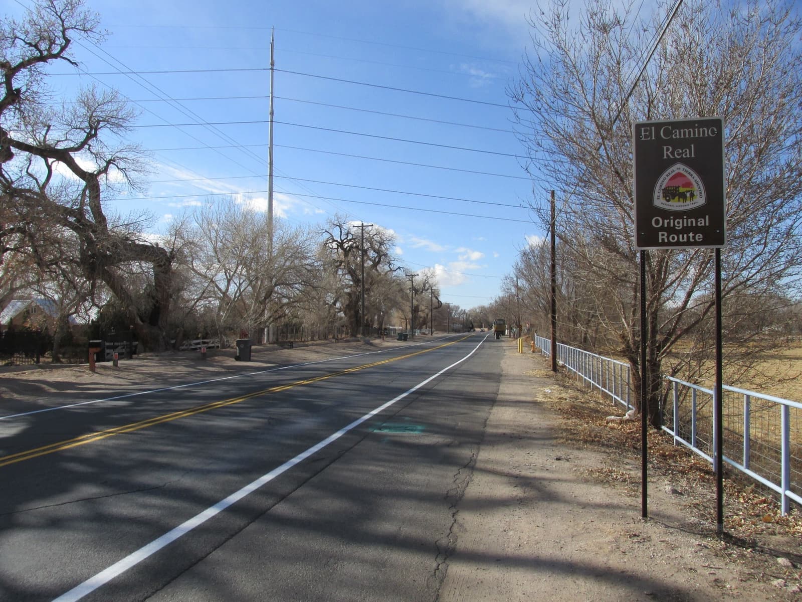 A two-lane road through bare cottonwoods with a historic route sign