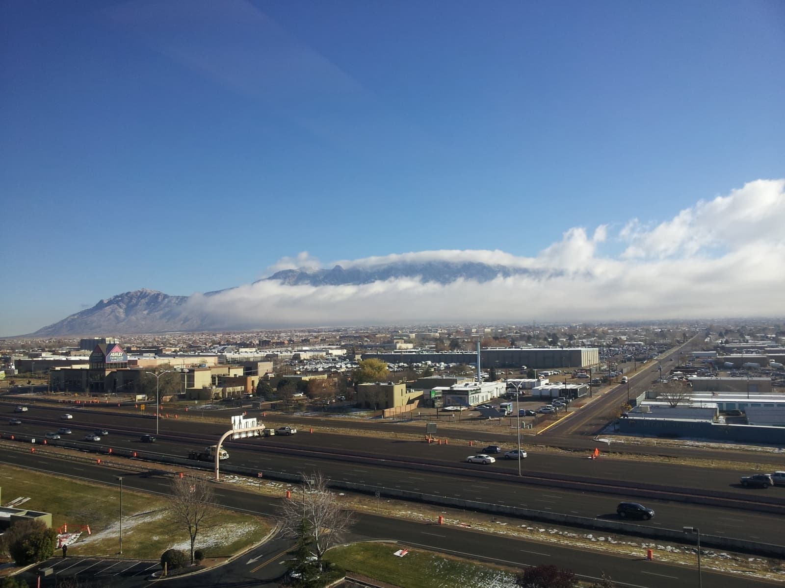 Freeway lanes and office blocks under the Sandia Mountains with cloud on the crest