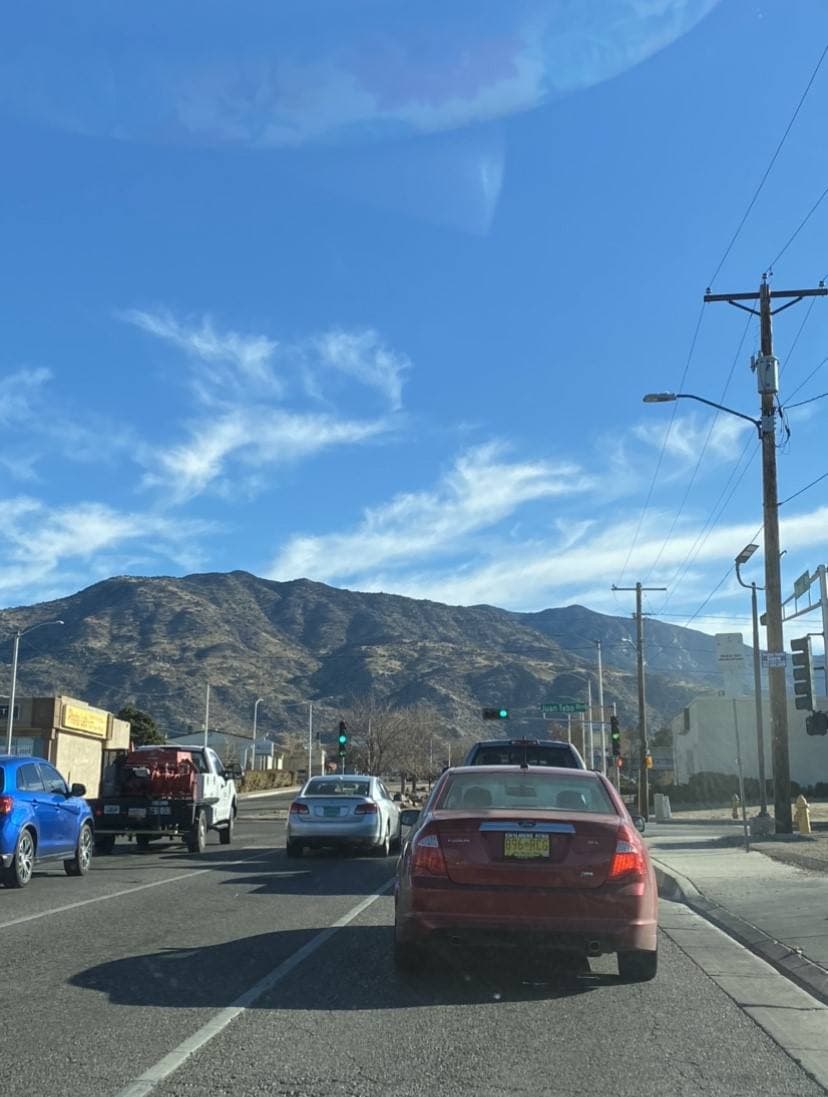 A wide suburban boulevard at a traffic light with the Sandia Mountains rising behind