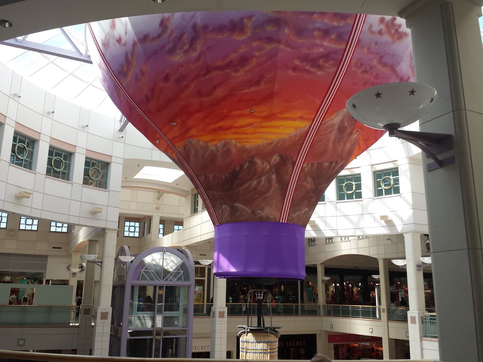 A two-level mall atrium under a skylight with a painted hot-air-balloon sculpture