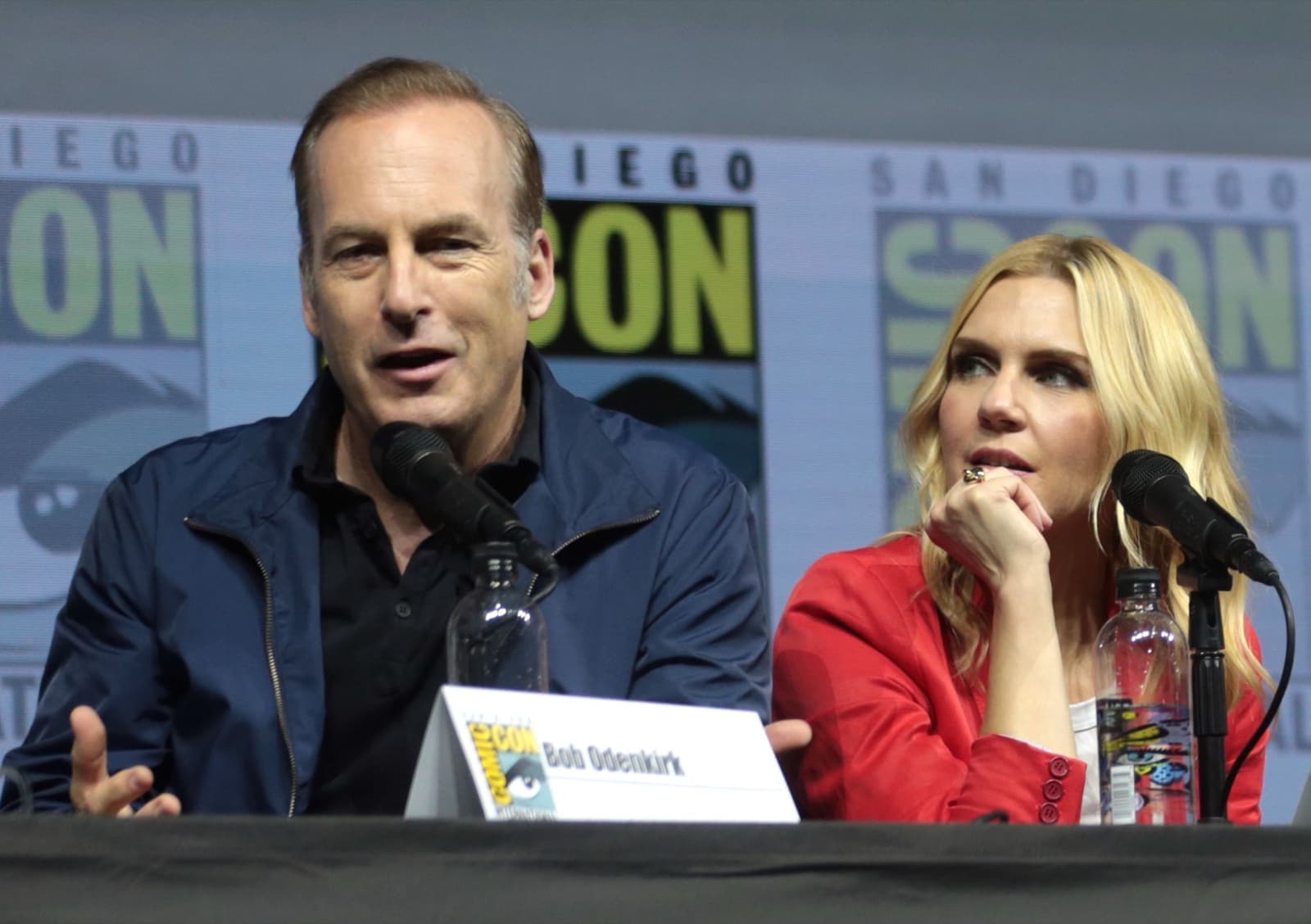 Bob Odenkirk speaking into a microphone beside Rhea Seehorn on a convention panel