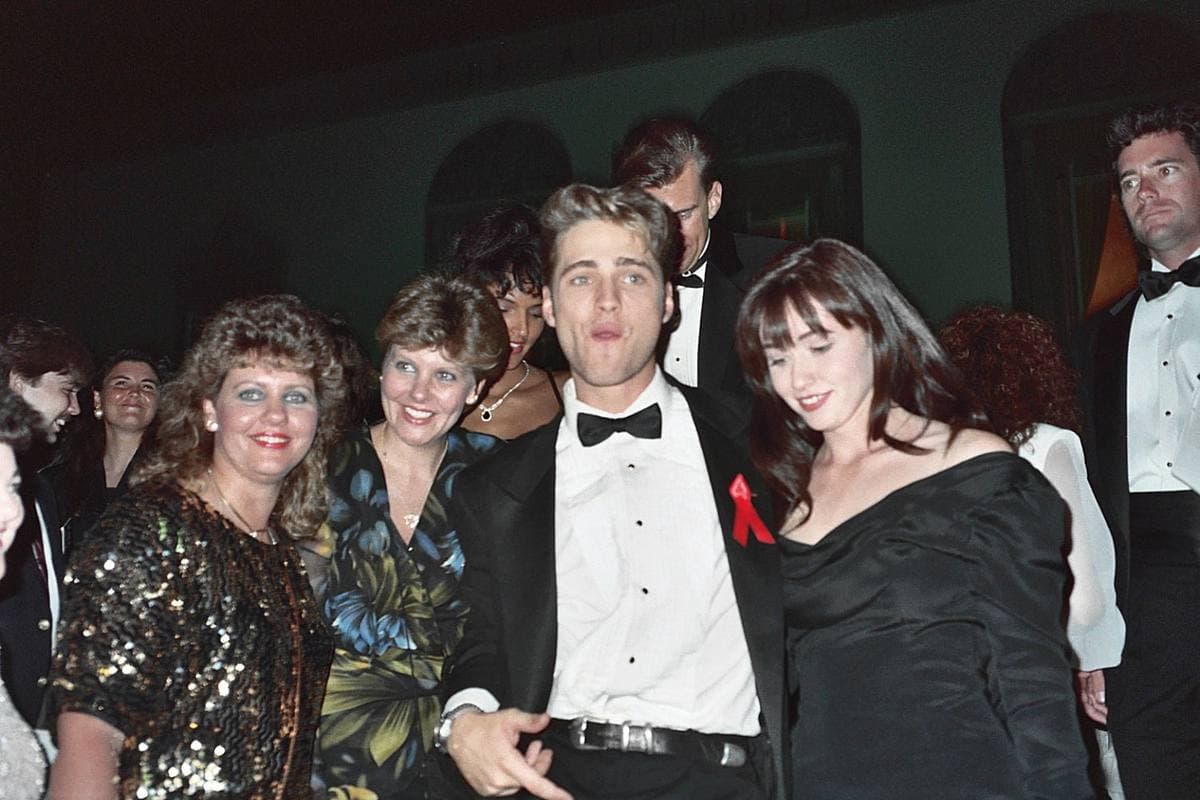 Jason Priestley and Shannen Doherty smiling among fans at an evening party