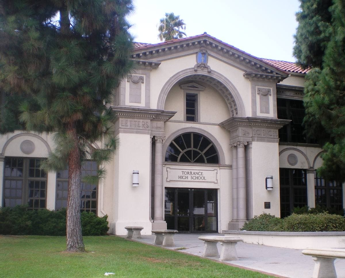 Arched Renaissance-style entrance of a pale two-storey school building with palm trees