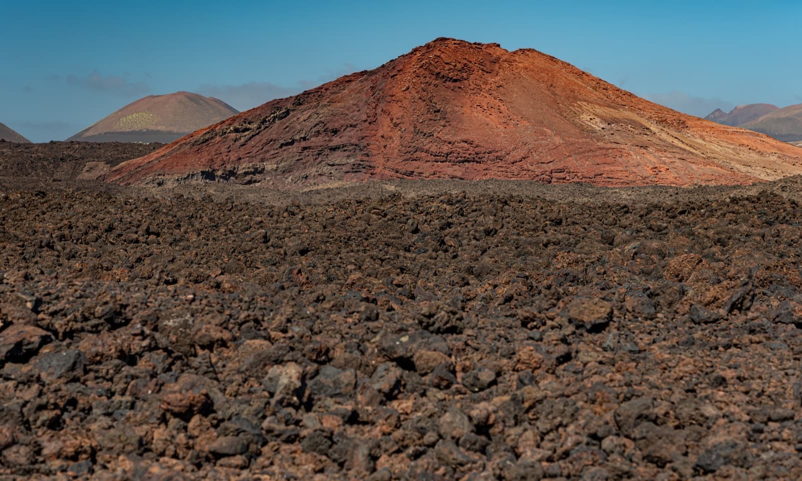 A rust-red volcanic cone rising over a black lava field