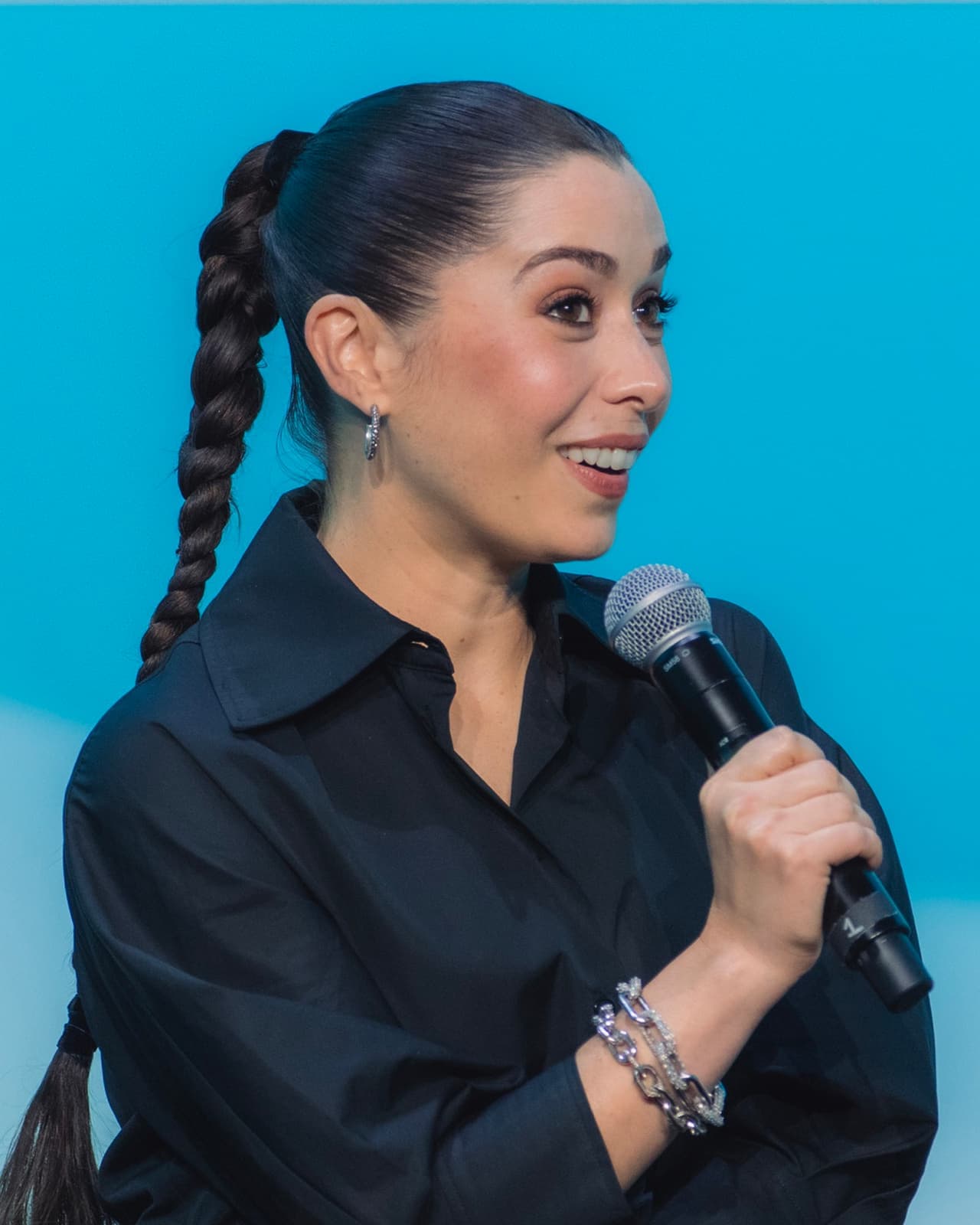 Cristin Milioti holding a microphone, in a black shirt, with her hair in a long braid