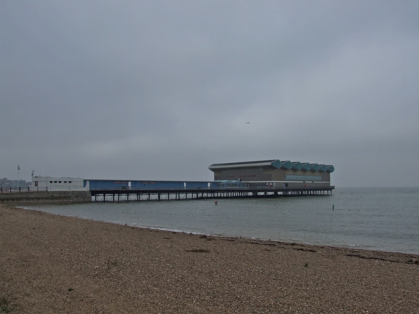 The detached pier head of Herne Bay standing out at sea beyond a shingle beach