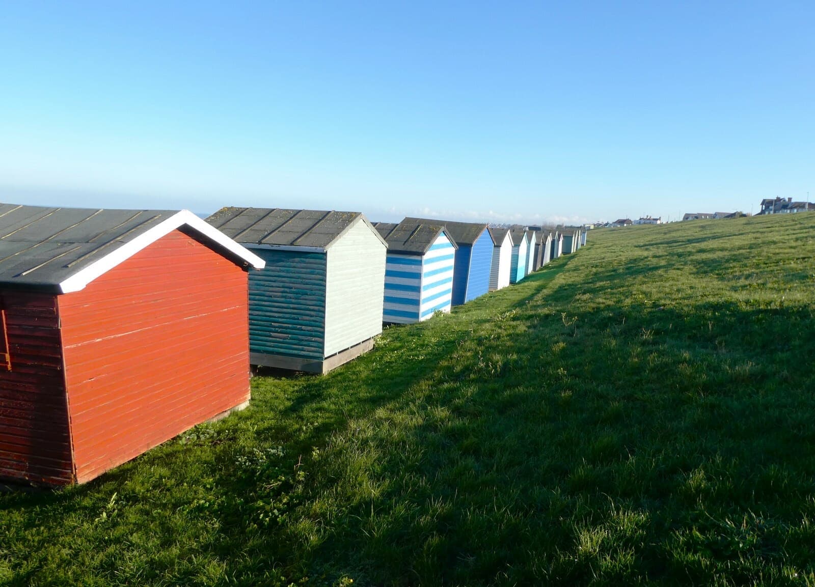 A row of coloured beach huts along the grassy top of Tankerton Slopes