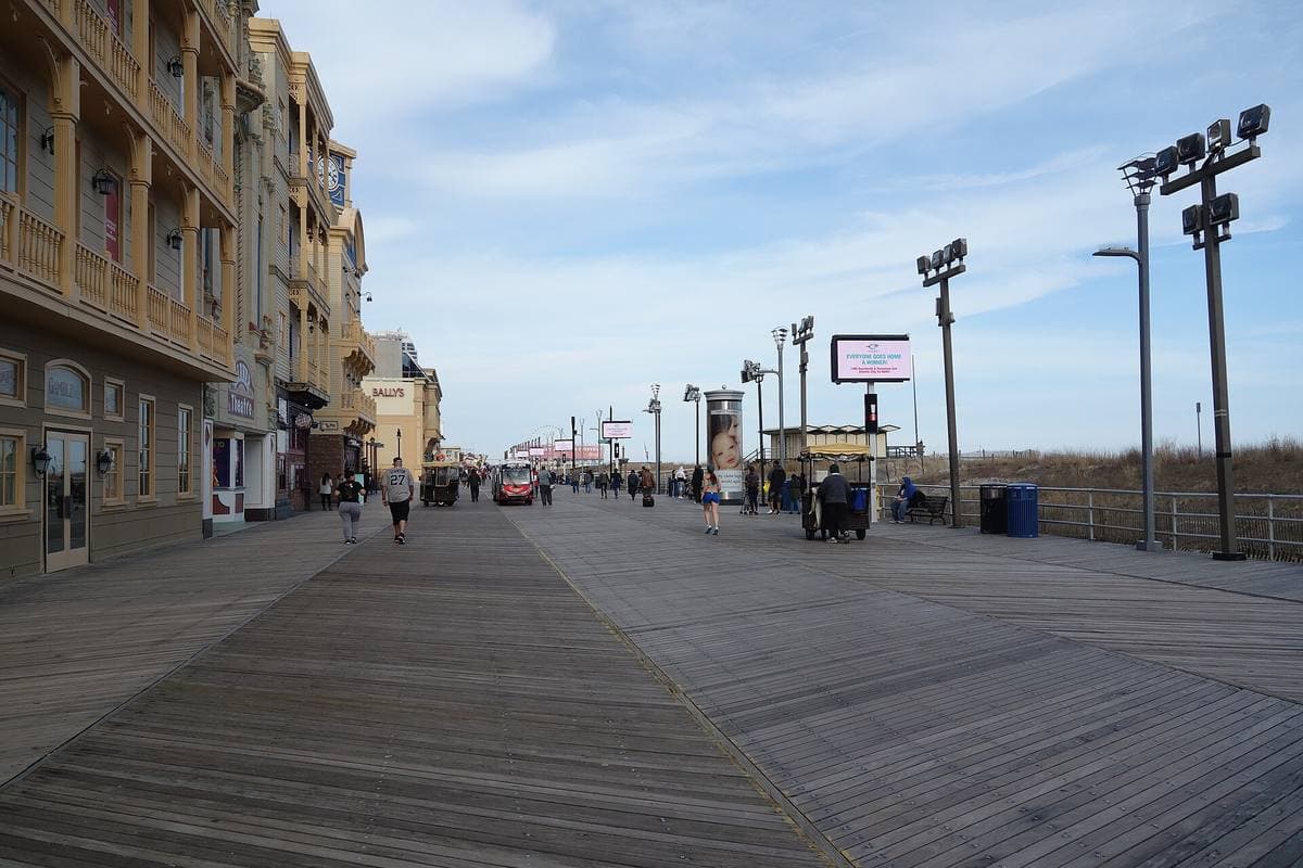 A wide wooden boardwalk with lamp posts, hotels on one side and dunes on the other