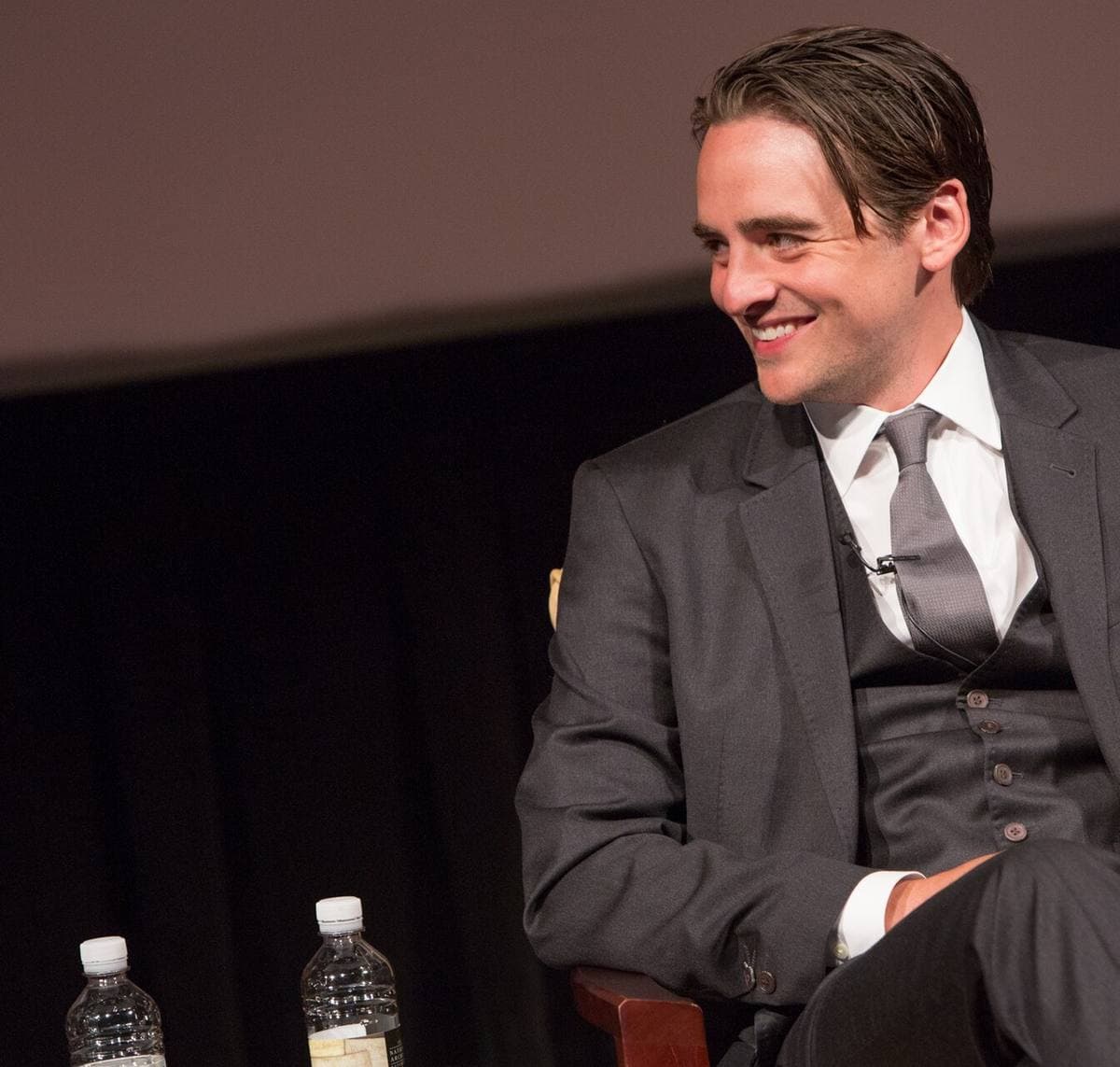 Vincent Piazza in a grey suit, laughing in an armchair