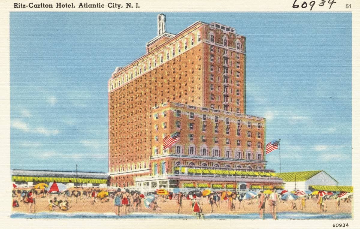 A coloured postcard of a tall brick hotel above a beach of umbrellas
