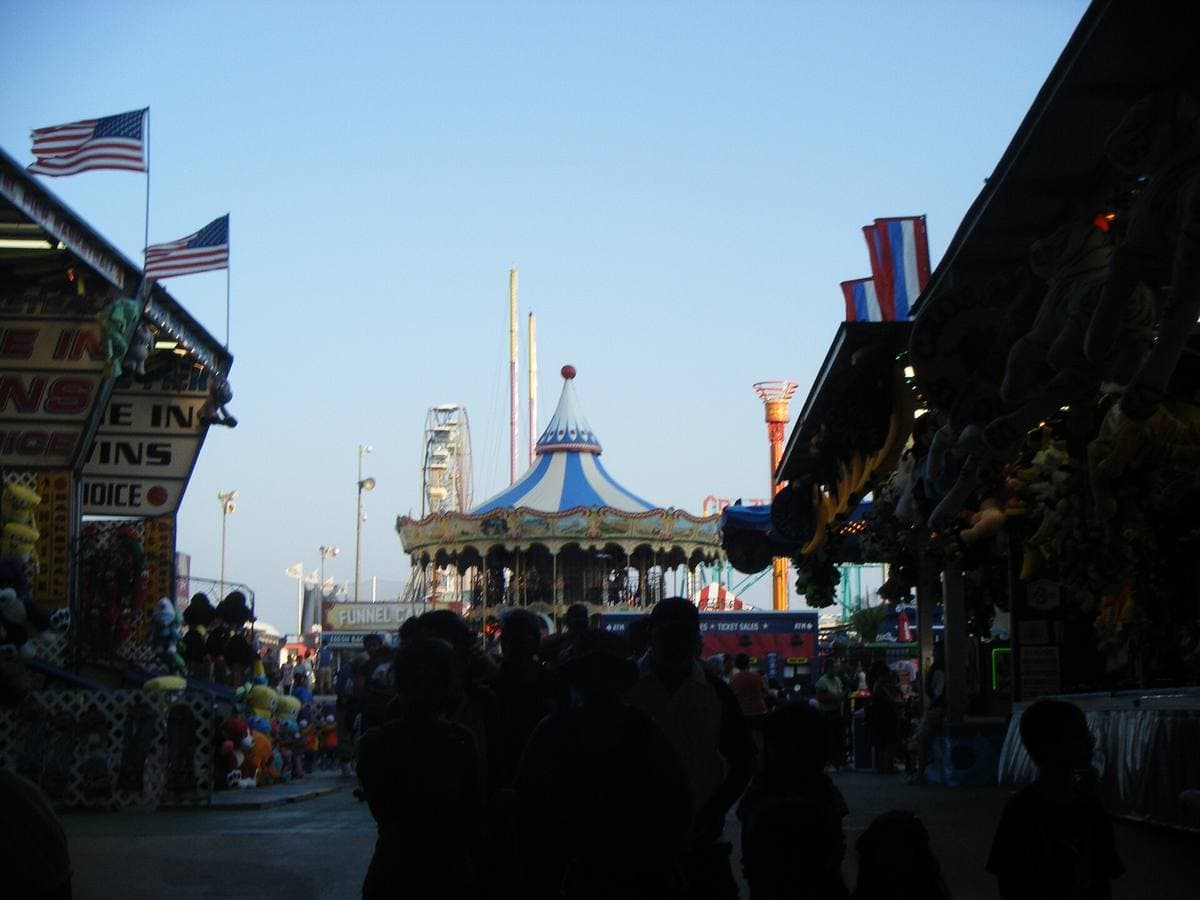 A pier lined with ride booths and flags, a carousel ahead