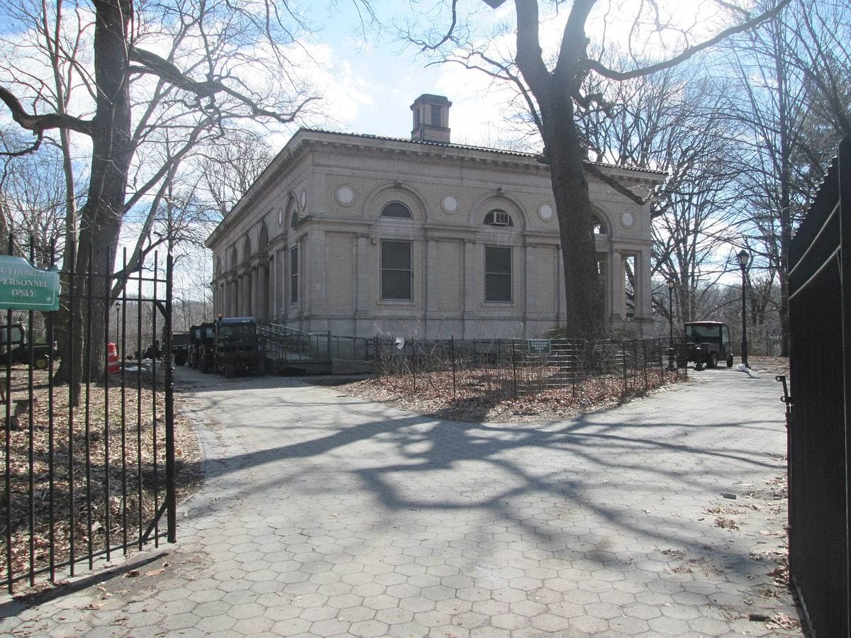 A pale classical pavilion behind iron railings in a winter park