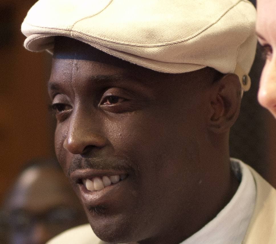 Michael K. Williams in a cream flat cap, smiling