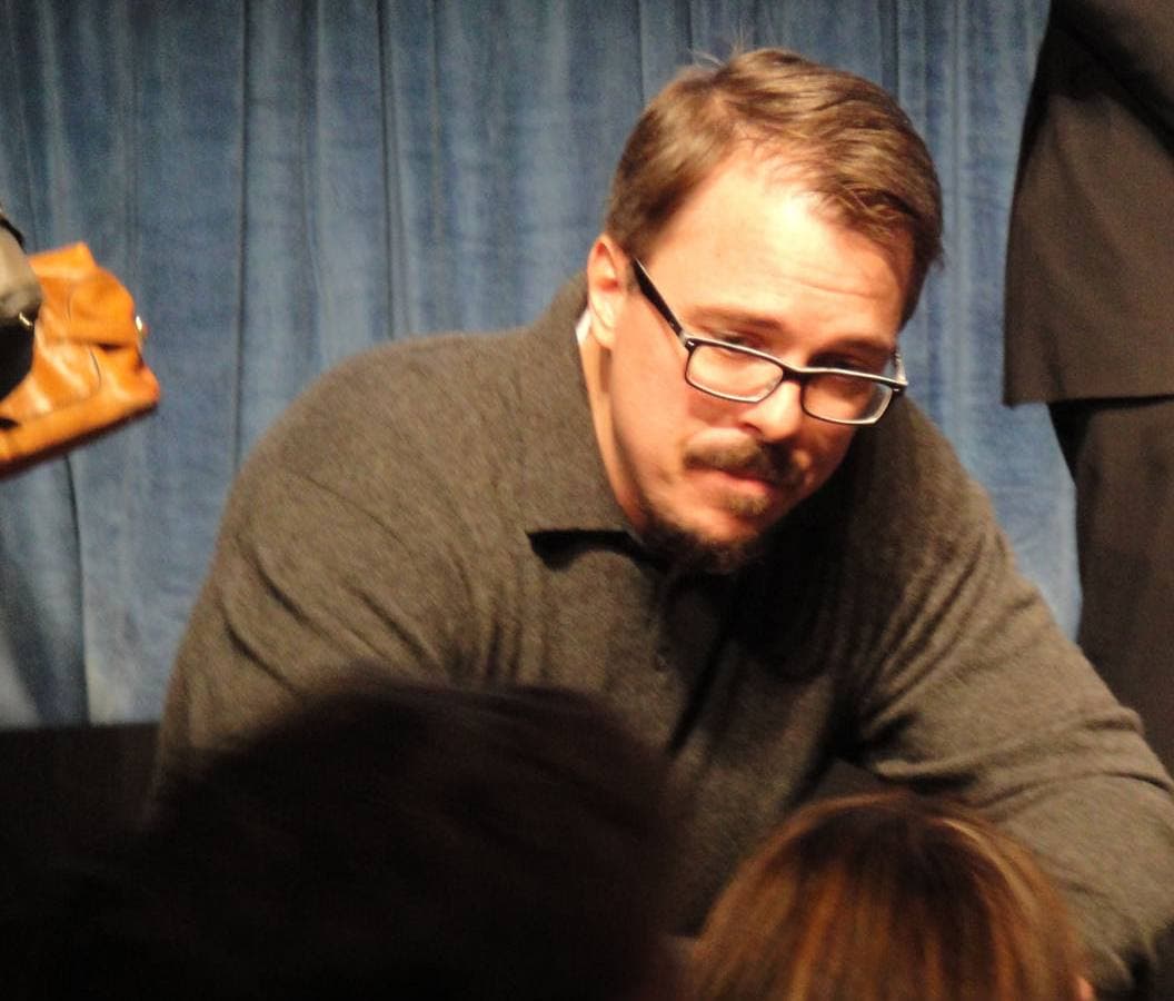 Vince Gilligan in glasses and a grey sweater, leaning down to fans