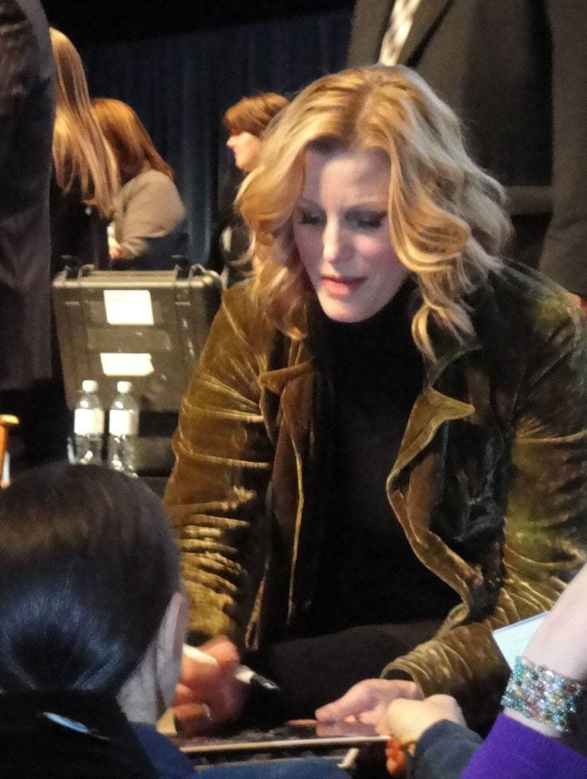 Anna Gunn, blonde, in a dark velvet jacket, signing autographs