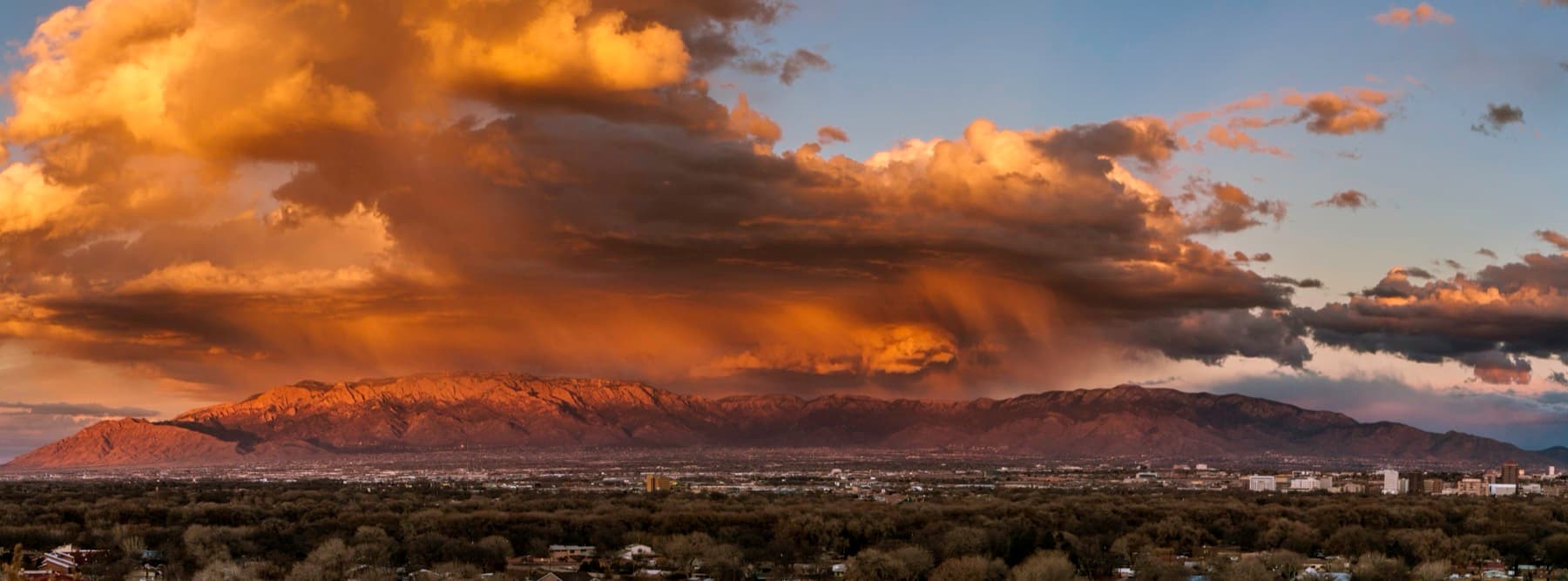 The city spread below a long mountain ridge turning pink at sunset