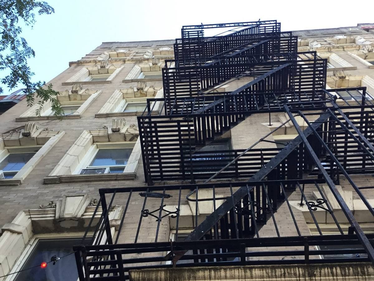 Looking up at a black iron fire escape on a pale tenement front