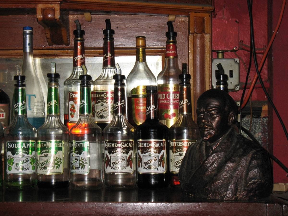 A dim red bar interior with a bust on a shelf above bottles
