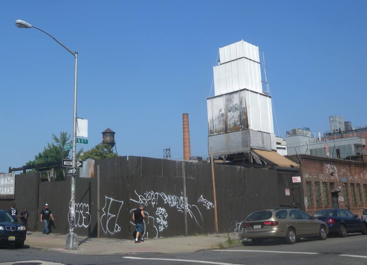 A Williamsburg street corner with a wooden water-tank factory on a sunny afternoon