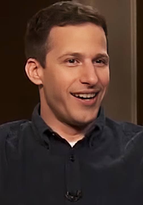 A smiling dark-haired man in a dark jacket, mid-interview