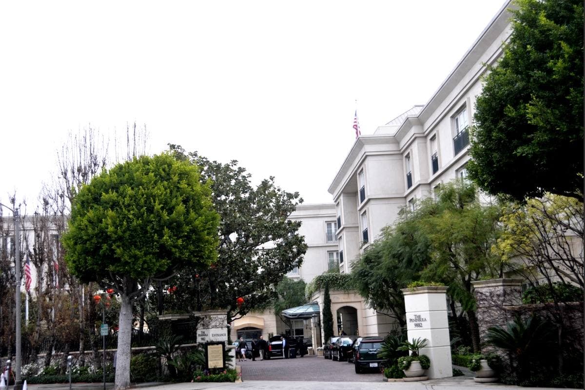 The cream entrance front of a hotel behind palms and a fountain
