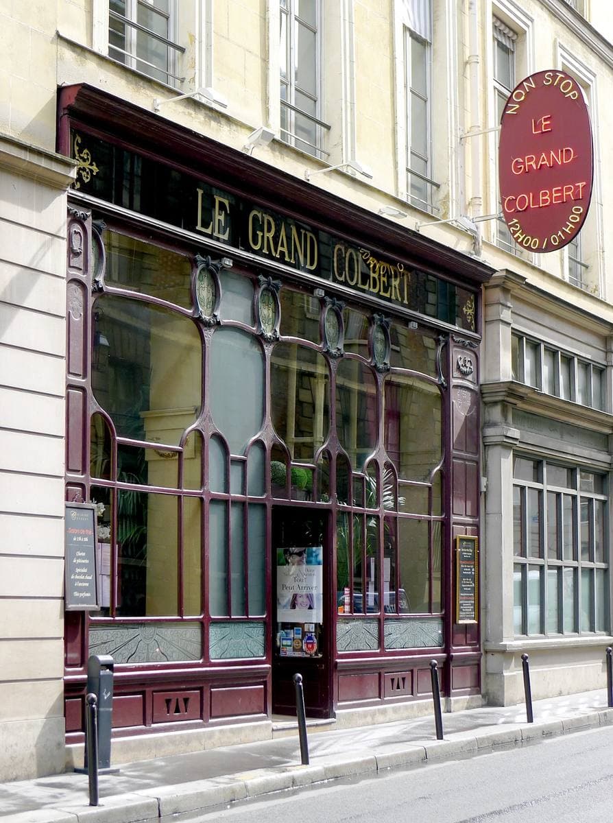 A brasserie front in dark red wood and glass, LE GRAND COLBERT above the door
