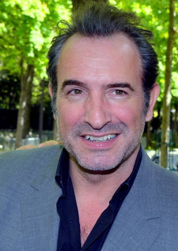Jean Dujardin grinning in an open-necked shirt and grey jacket