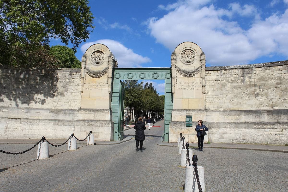 A walled cemetery gateway with two stone pillars under a blue sky