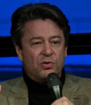 Thibault de Montalembert speaking into a microphone, in a dark jacket
