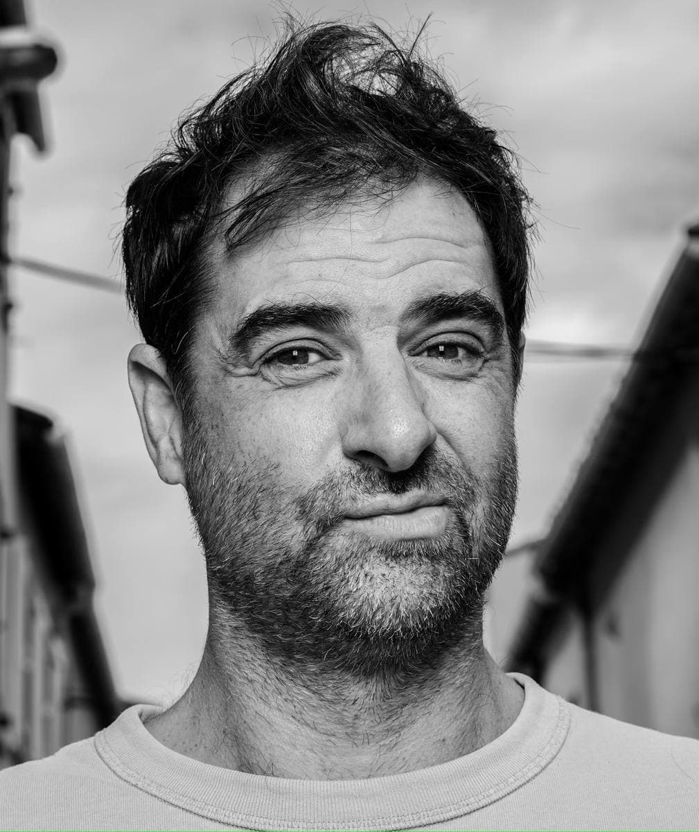 Grégory Montel in black and white, unshaven, looking into the camera