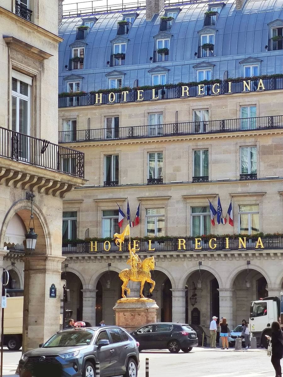 A Paris hotel front with HOTEL REGINA in gold, a gilded equestrian statue before it