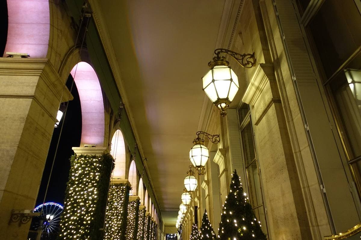 A stone arcade with hanging lanterns and a Christmas tree, lit in pink